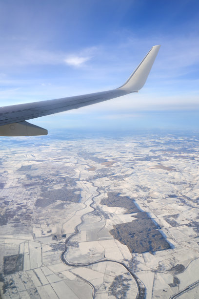 飞行和旅行。日落时从机翼上的飞机窗户看到的景色。冬天，飞机在陆地上飞行。图片下载