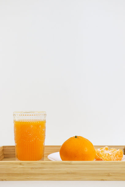 一杯自制的天然榨汁橙汁，加上一个完整的橙汁和一些去皮的橙片放在一个木制托盘里，后面是白色的背景图片下载