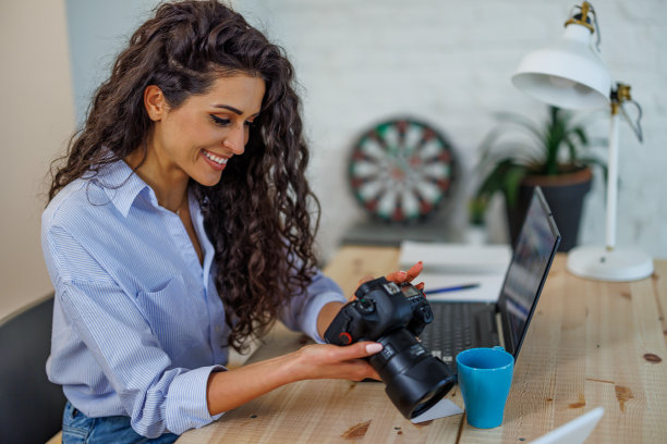 自由摄影师年轻女子与相机在家里办公室编辑照片的电脑图片下载
