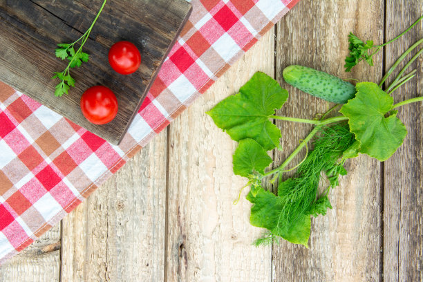 带叶子的新鲜黄瓜和圣女果放在格子厨房毛巾，木桌上。照片图片下载
