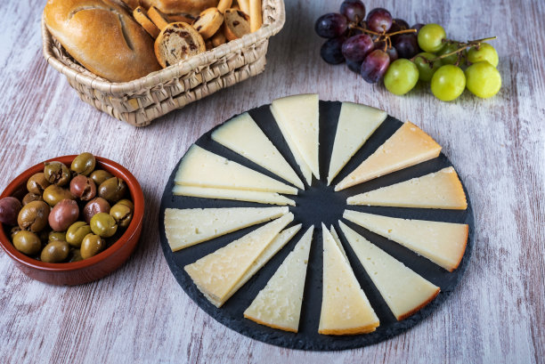 切成楔形的西班牙奶酪板，放在质朴的石头盘子上，配以葡萄、橄榄和面包。图片下载