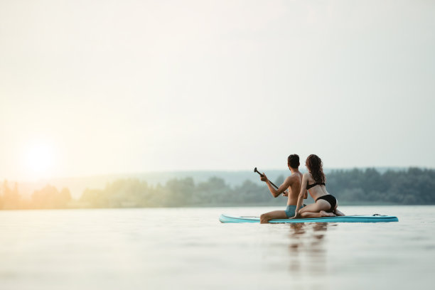 一对年轻的夫妇沿着河散步，坐在SAP板上图片下载
