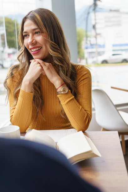 女人微笑着与一个开放的书在餐厅的桌子上，拉丁年轻女子与长金发，生活方式图片下载