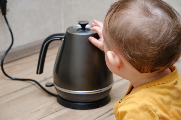 蹒跚学步的小男孩拿着一个盛着开水的热水壶。孩子的安全问题在家里，小孩子图片下载