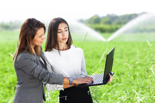 在有农业灌溉系统的田地里，拿着笔记本电脑的女商人。图片下载