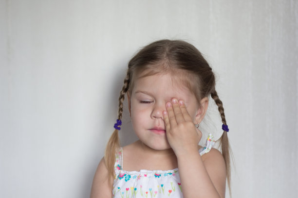 肖像的孩子与闭上眼睛和手握她的左眼在白色的背景图片下载