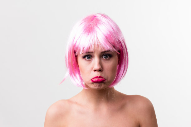 一个年轻女子的脸与明亮的化妆品在粉红色的背景聚集的头发在一个光滑的马尾。图片下载