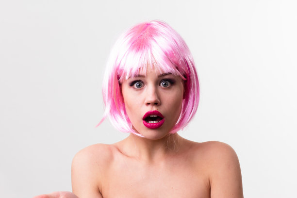 一个年轻女子的脸与明亮的化妆品在粉红色的背景聚集的头发在一个光滑的马尾。图片下载