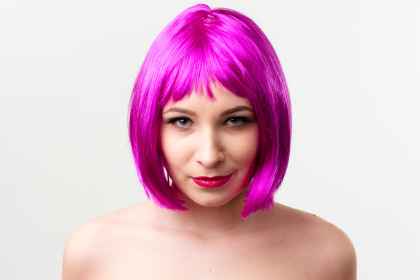 一个年轻女子的脸与明亮的化妆品在粉红色的背景聚集的头发在一个光滑的马尾。图片下载