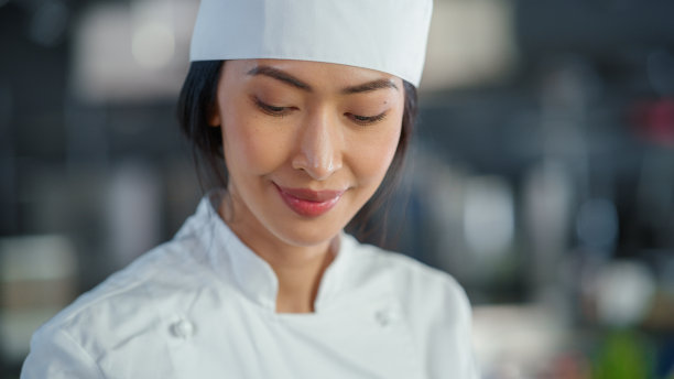 世界著名餐厅:微笑的亚洲女厨师的肖像烹饪美味，蒸汽，正宗的食物，在厨房使用数字平板电脑。准备负担得起的高级美食。图片下载