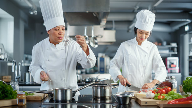世界著名餐厅:由亚洲和黑人女厨师组成的双人团队，烹饪美味地道的食物，完美的团队合作，在现代厨房里准备健康的饭菜。融合料理大师。广角镜头图片下载