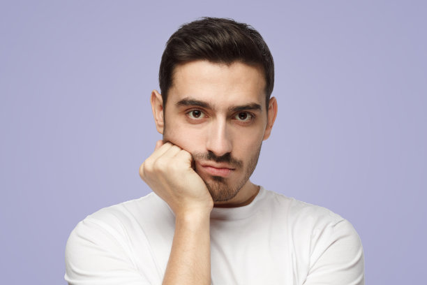 年轻人把手压在下巴上，看起来无聊，疲惫和失望，感到无助图片下载
