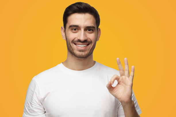 穿着白色t恤的年轻人看起来很开心，微笑着，打手势，显示OK的迹象图片下载