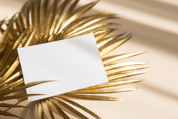 邀请卡模型与金色棕榈叶米色粉彩背景。俯视图，平面布局，复制空间。模板空白的白纸模型为品牌和广告图片下载