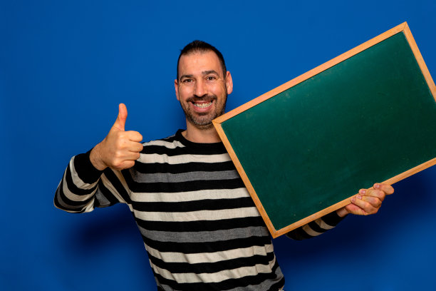 快乐的大胡子西班牙人显示，呈现和持有空白的白板与拇指向上孤立在蓝色背景图片下载
