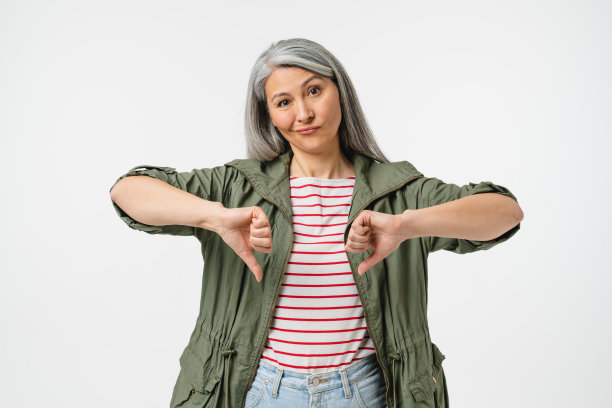 悲伤失望的成熟中年白人妇女与灰色头发显示拇指向下的分歧孤立在白色背景。消极的态度图片下载