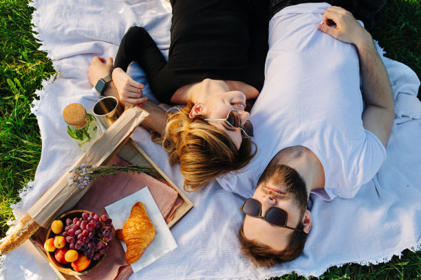 野餐时，一对幸福的夫妇躺在毯子上，旁边是食物盒图片下载