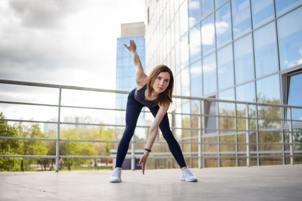 年轻的健身女子在城市建筑附近做热身运动。健康的生活方式图片下载
