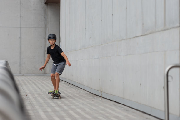 戴着头盔的黑发少女在混凝土建筑前的站台上玩滑板图片下载