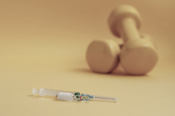 注射器和装有液体的医疗安瓿放在哑铃前面的黄色背景上，复制空间。兴奋剂的概念是指在体育运动中禁用的类固醇、睾丸激素等药物。图片下载