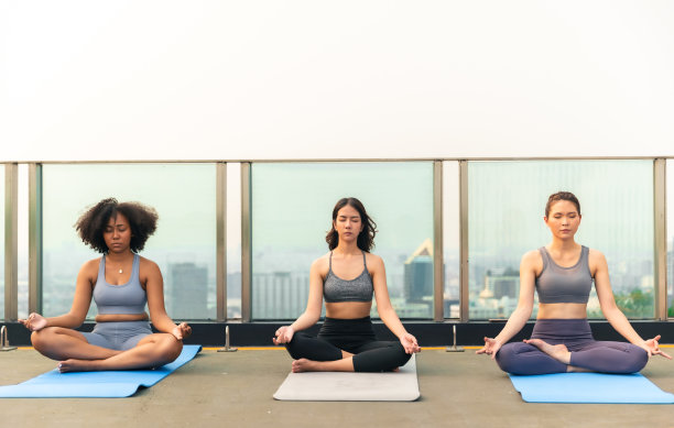 年轻的亚洲女性和非裔美国人在屋顶上练习瑜伽。一群快乐的健身朋友在城市户外锻炼。图片下载