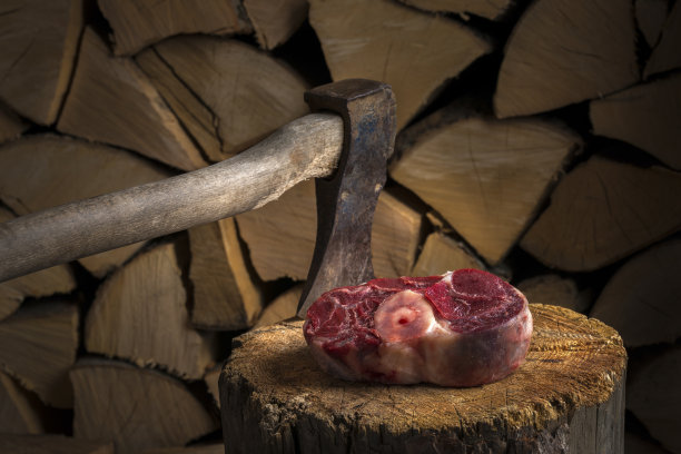 木斧插在厚牛排上，还有篝火。在满是烧烤木柴的柴棚前。图片下载