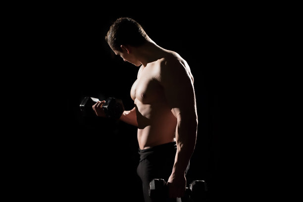 英俊的力量运动员男子健美运动员做练习与哑铃。健身肌肉的身体在黑暗的背景图片下载