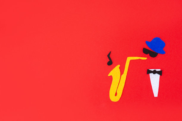 爵士乐的一天。一个音乐家的剪影，在红色的背景上，用毛毡剪下，吹着萨克斯管，旋律从里面飞出来。平的。本空间图片下载