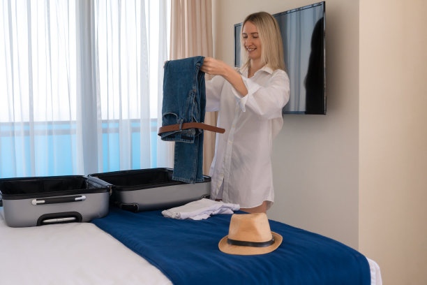 穿着白衬衫的快乐的年轻女子收集或打开箱子里的东西躺在床上。旅游、度假的概念图片下载