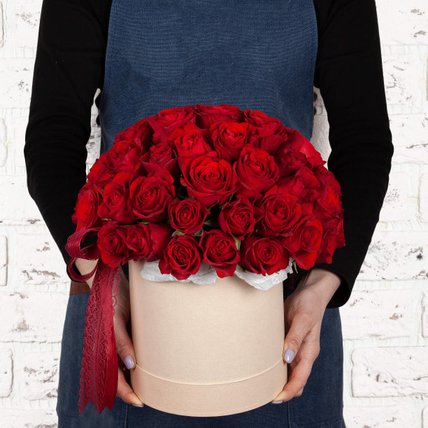 女花商持有新鲜的鲜花盛开的红色花束在盒子上的砖墙背景图片下载