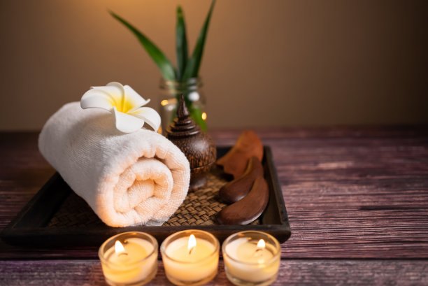 靠近木制枪沙，卷毛巾，石头，花和蜡烛在托盘上的木制背景。面部spa套装，健康安康的生活理念。图片下载