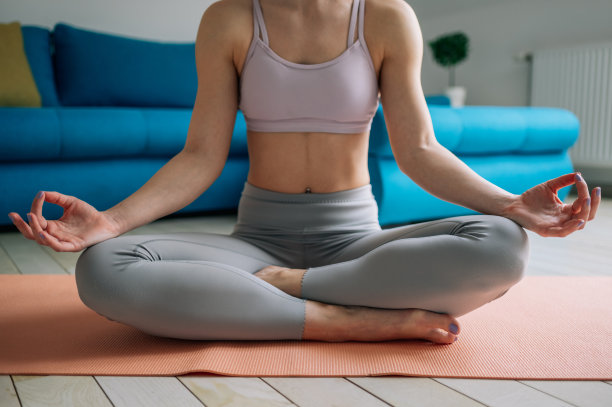 女人坐在一个莲花瑜伽的位置在健身垫上在家里图片下载
