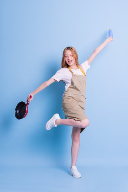 在蓝色背景上拿着平底锅的年轻亚洲女人的形象图片下载