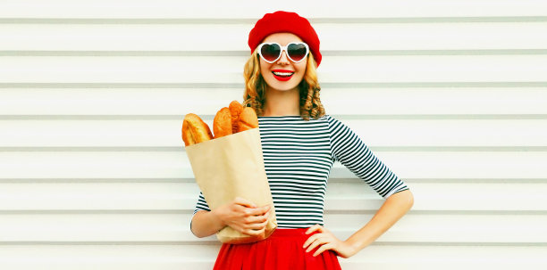 幸福微笑的年轻女子的肖像戴着法国红色贝雷帽持有纸袋与长白面包法棍在白色背景图片下载