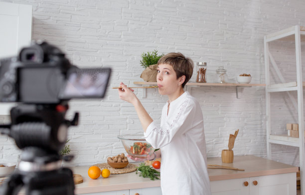 一个年轻漂亮的博客女孩正在录制一个视频教程，烹饪沙拉在家庭厨房。图片下载