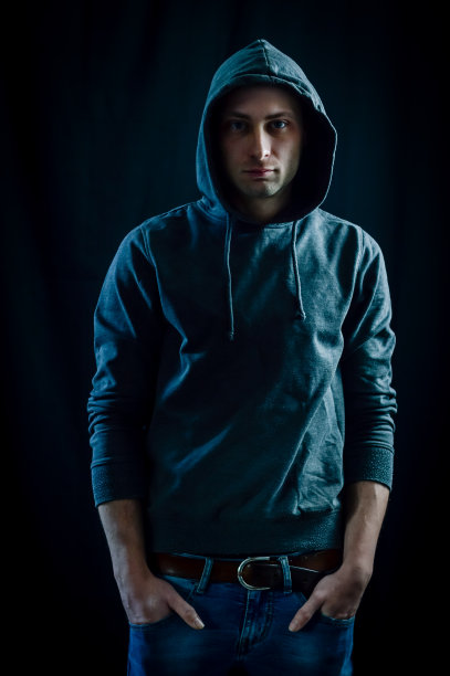 一个英俊的年轻男子的肖像，蓝眼睛兜帽他的手在他的牛仔裤口袋图片下载