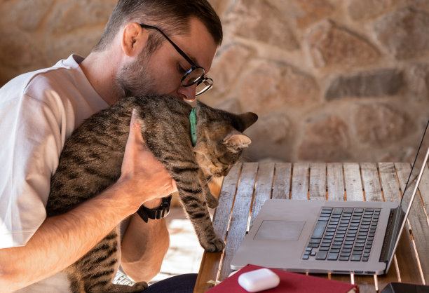 有魅力的年轻成年男子在使用笔记本电脑时手里拿着一只猫。图片下载