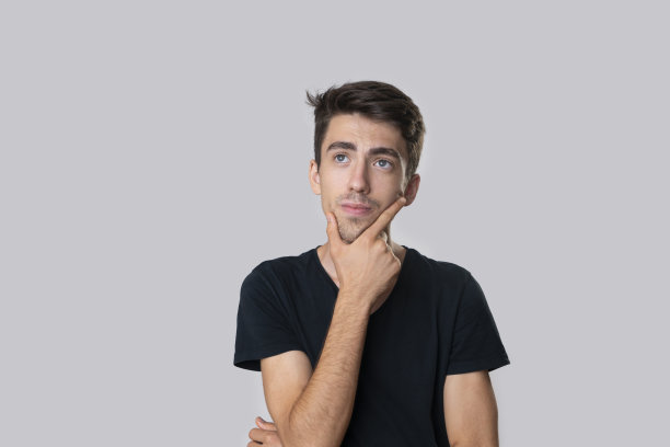 一个穿着黑色衬衫的年轻人的肖像，正在思考着什么，摄影棚拍摄，灰色的背景。图片下载