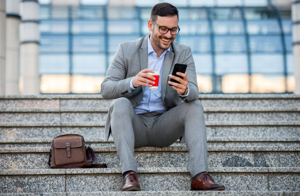 商人坐在公司前，喝着咖啡，用智能手机查看数据。商业、教育、生活理念图片下载