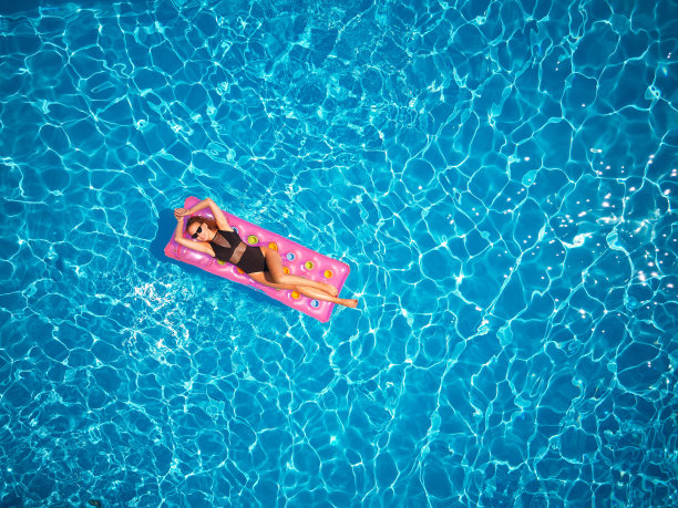 穿着比基尼的漂亮女孩在游泳池的充气粉色床垫上冷却。苗条火辣的女人在泳装晒黑。女放松漂浮在蓝色的水在豪华度假村。航拍，从上面看图片下载