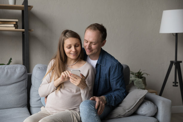 快乐的年轻未来父母在家使用手机。图片下载