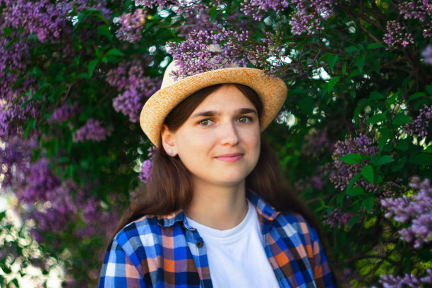 春天的女人。离焦点美丽的年轻女子附近盛开的春天树。布什淡紫色的花。青春、爱情、时尚、浪漫、生活理念。在自然背景下戴帽子的女孩。的焦点图片下载