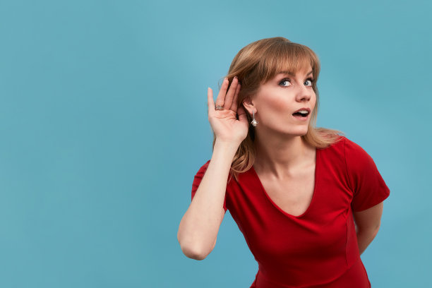 一个迷人的长发年轻女护士的肖像你说什么标志把她的手放在她的耳朵穿着红色的手术服图片下载