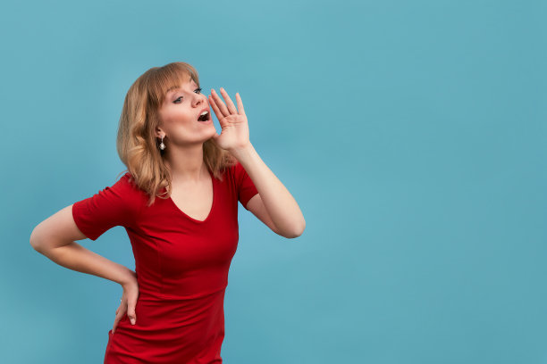 年轻女子把手放在脸上，对着一个孤立在蓝色背景下的人大喊。复制，空出文本图片下载