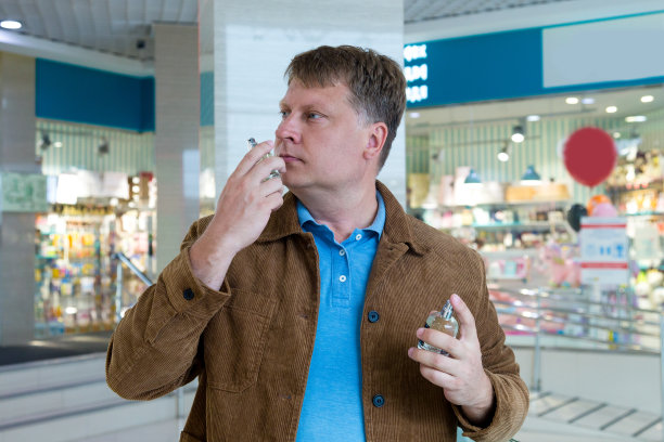 一个金发的成年男子在购物中心手里拿着一个瓶子，试图捕捉香水的味道图片下载