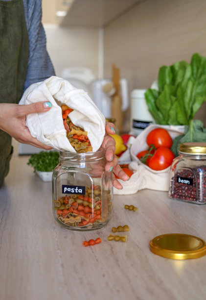 一名年轻的亚洲女子正在把意大利面从袋子里倒进玻璃罐里。硬质小麦品种。图片下载