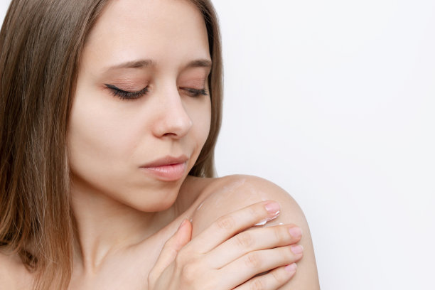 一个年轻迷人的白种金发女人按摩她的肩膀保湿她的皮肤图片下载