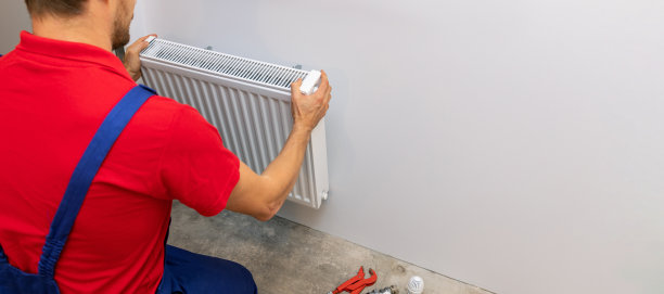 有人在墙上安装白色金属散热器。住宅供暖系统。本空间图片下载