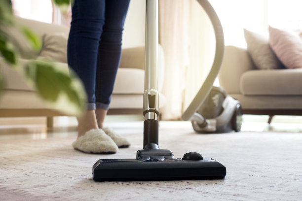 年轻女子在家里用吸尘器清洁地毯。图片下载
