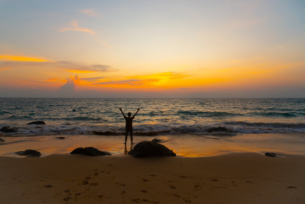 一名男子在海滩上举起手臂，争取成功图片下载